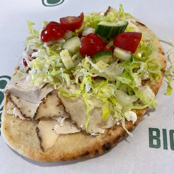 A turkey pita with lettuce, tomatoes, cucumbers, and feta cheese on a white background.