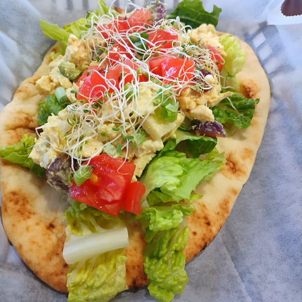 A Bigfoot Subs pita sandwich filled with chicken salad, lettuce, tomatoes, and sprouts.