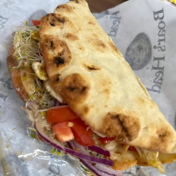 Bigfoot Subs sandwich with sprouts, tomatoes, red onions, and melted cheese on flatbread.