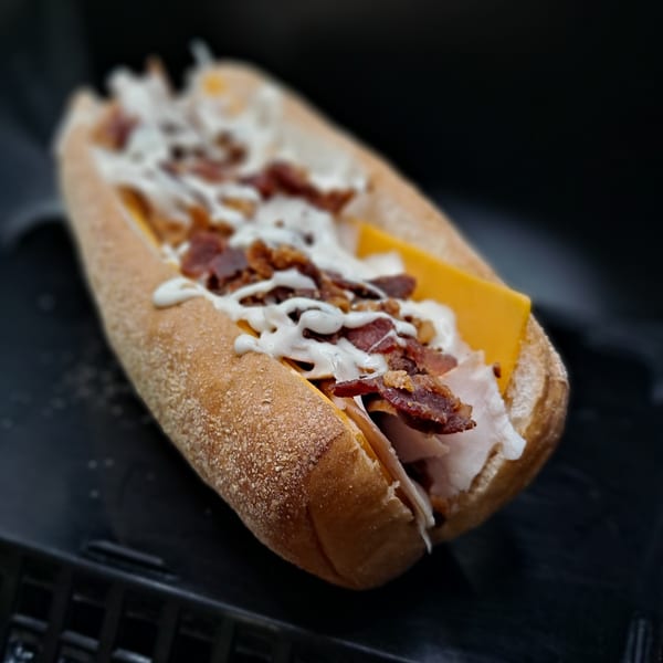 A Bigfoot Subs sandwich filled with turkey, cheese, bacon, and white sauce on a dark background.