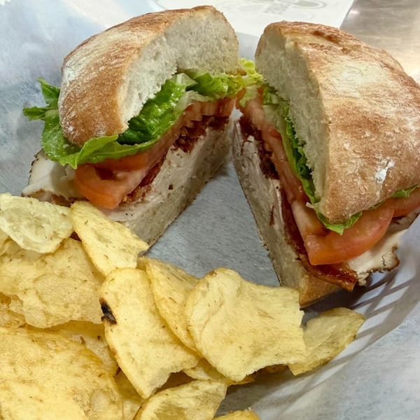 A turkey club sandwich, cut in half, with lettuce, tomato, and bacon, served with potato chips.